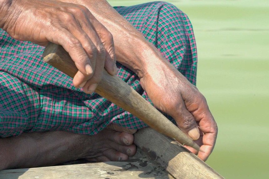 U Maung Lay's lands tap a wooden stick against the boat