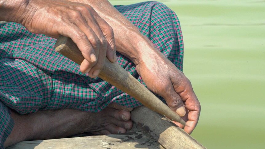 U Maung Lay's lands tap a wooden stick against the boat