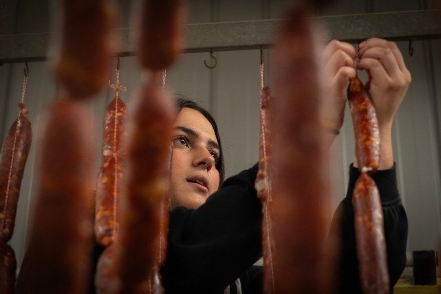 A woman hangs up stringed up sausages to dry