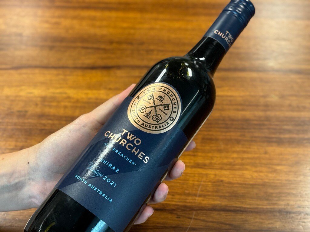 A hand holding a bottle of wine with the label Two Churches shiraz South Australia.
