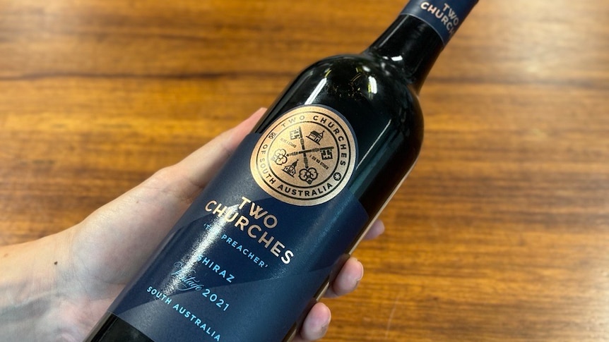 A hand holding a bottle of wine with the label Two Churches shiraz South Australia.