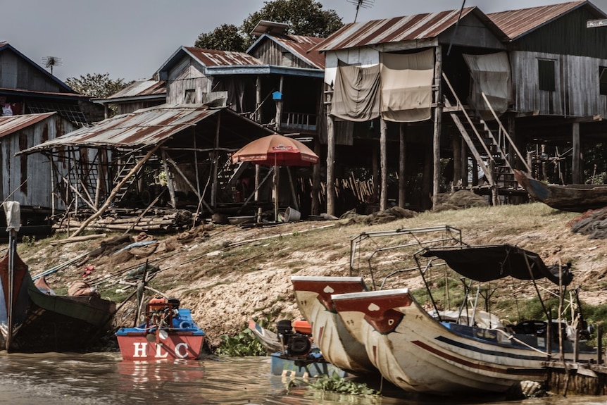 A group of shanty houses on stilts next to a river with boats