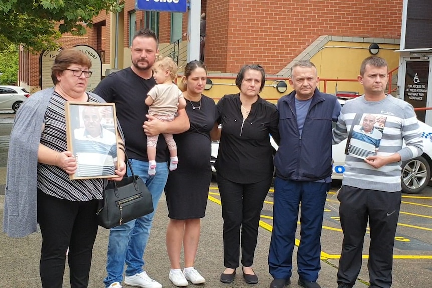 A family group stands outside a police station, holding pictures of a missing man.