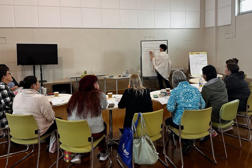 a woman stands in front of a group of other women writing on a whiteboard.