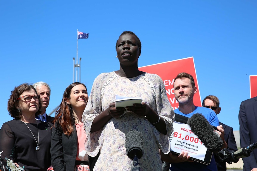 Ms Nyuon is flanked by supporters, including Labor MPs. She's holding a notebook, and the Parliament House flagpole is behind.