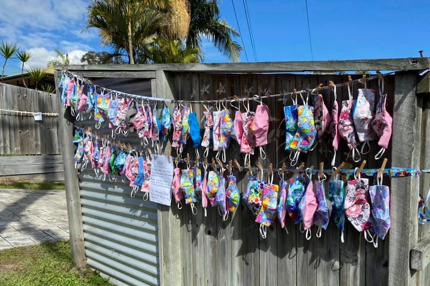 Two rows of brightly coloured masks hang from a fence.