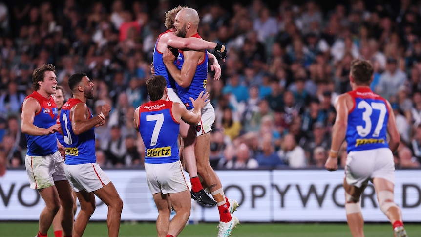 Melbourne's Max Gawn embraces in mid-air with a teammate as his team runs in to congratulate him after a goal. 