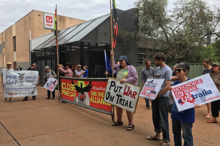 Protestors standing with signs that read: put war on trial, close Pine Gap