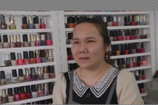 An Asian lady standing in front of a row of nail polish 