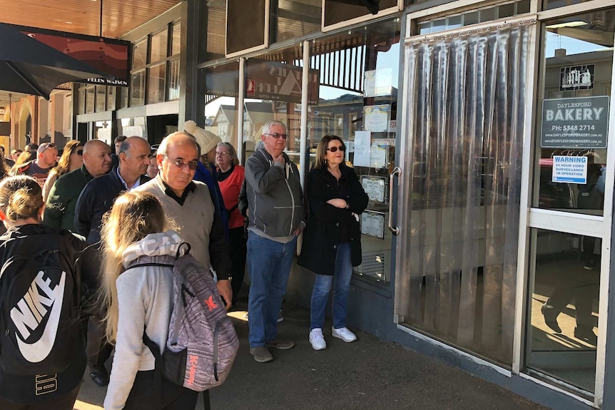People line up on a sunny day outside a local bakery waiting to be let in.