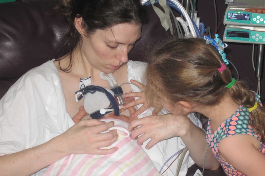 Rachel holds a very small Estelle while an older sibling looks on.