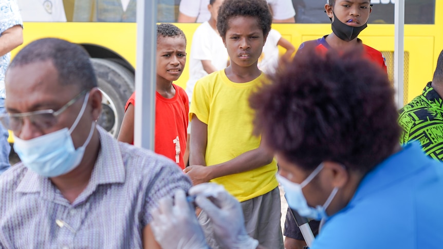 Three Papua New Guinean boys watch a man receive a needle in the arm 