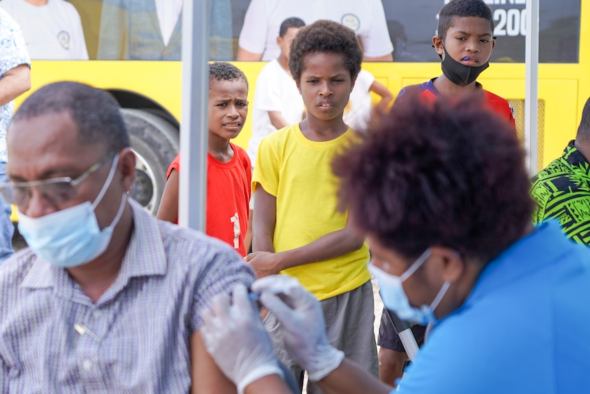 Three Papua New Guinean boys watch a man receive a needle in the arm 