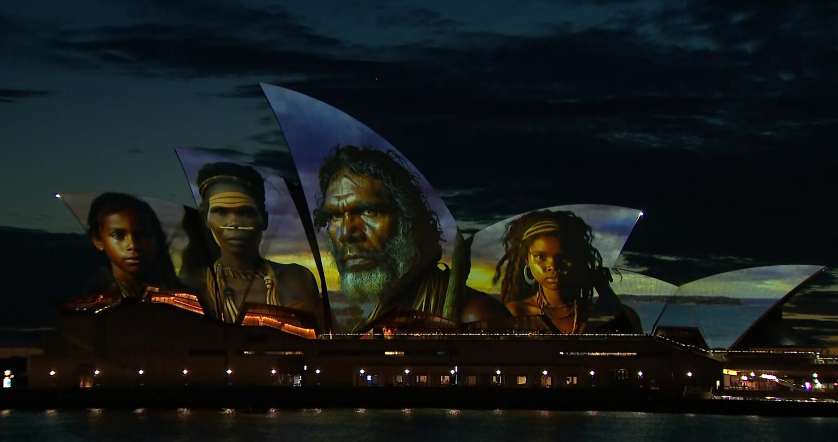 Four faces with a blue and yellow background are shown on a large sculputre.