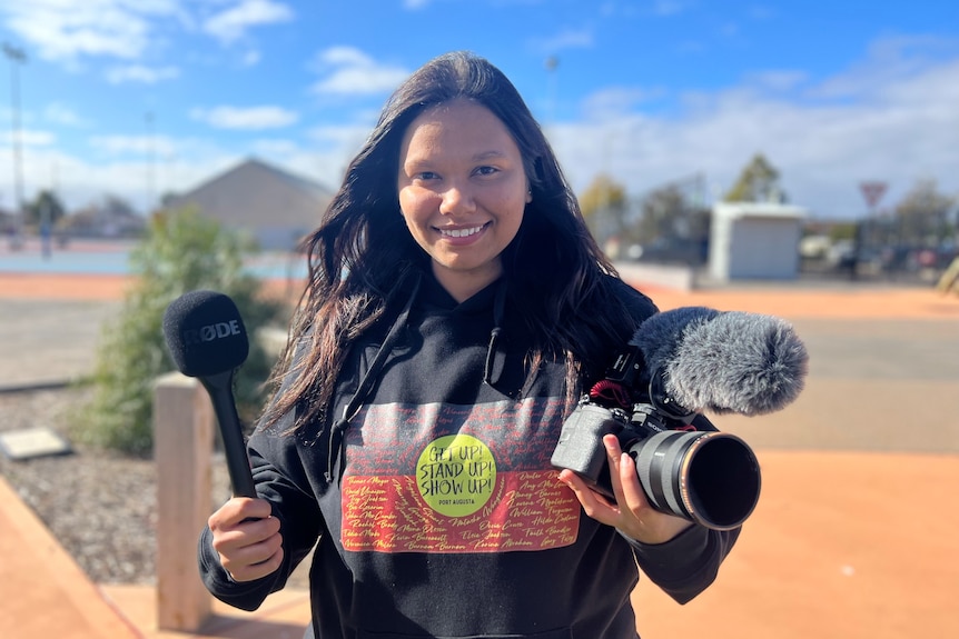 Journalist Chevon McKenzie holding a camera and microphone.