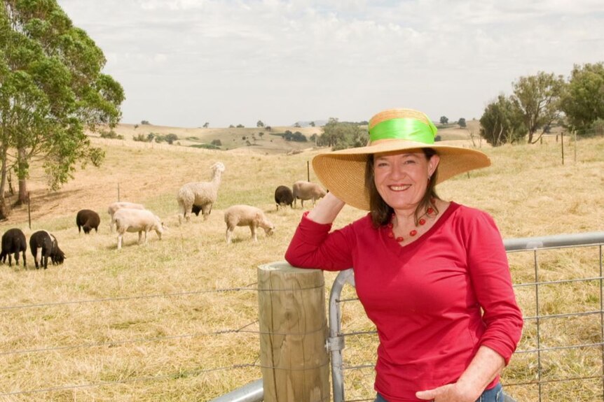 woman in dark pink three-quarter sleeve top wears wide-brim straw hat on farm