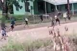 People running across a dirt road in a remote community in front of a house