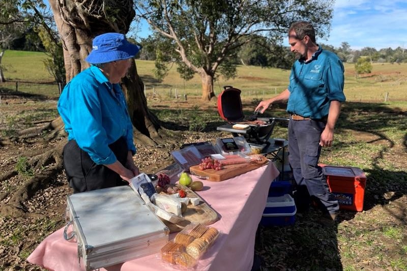 Photo of a man and a woman with a table of food and a BBQ.