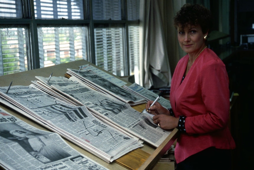 A young Ewart standing next to bench with newspapers on it early in her career.