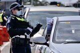 A police officer wearing a mask checks a permit being held by a driver at a check-point on a highway.