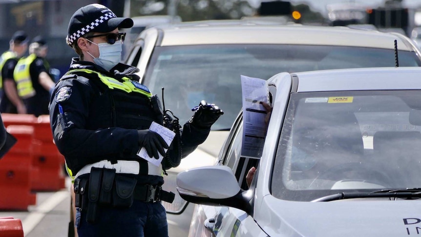 A police officer wearing a mask checks a permit being held by a driver at a check-point on a highway.