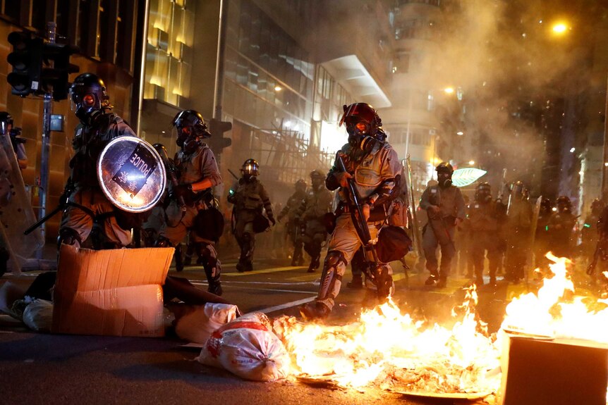 Heavily armed police stride through Hong Kong streets set alight with petrol bombs as riots continue.