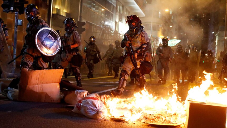 Heavily armed police stride through Hong Kong streets set alight with petrol bombs as riots continue.