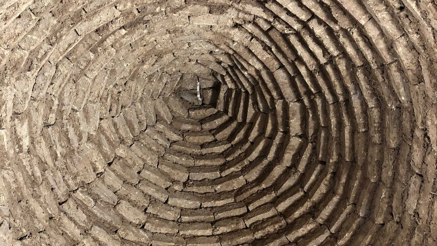Mud bricks carefully arranged in a circle, layered upwards in a staggered manner to create a dome.
