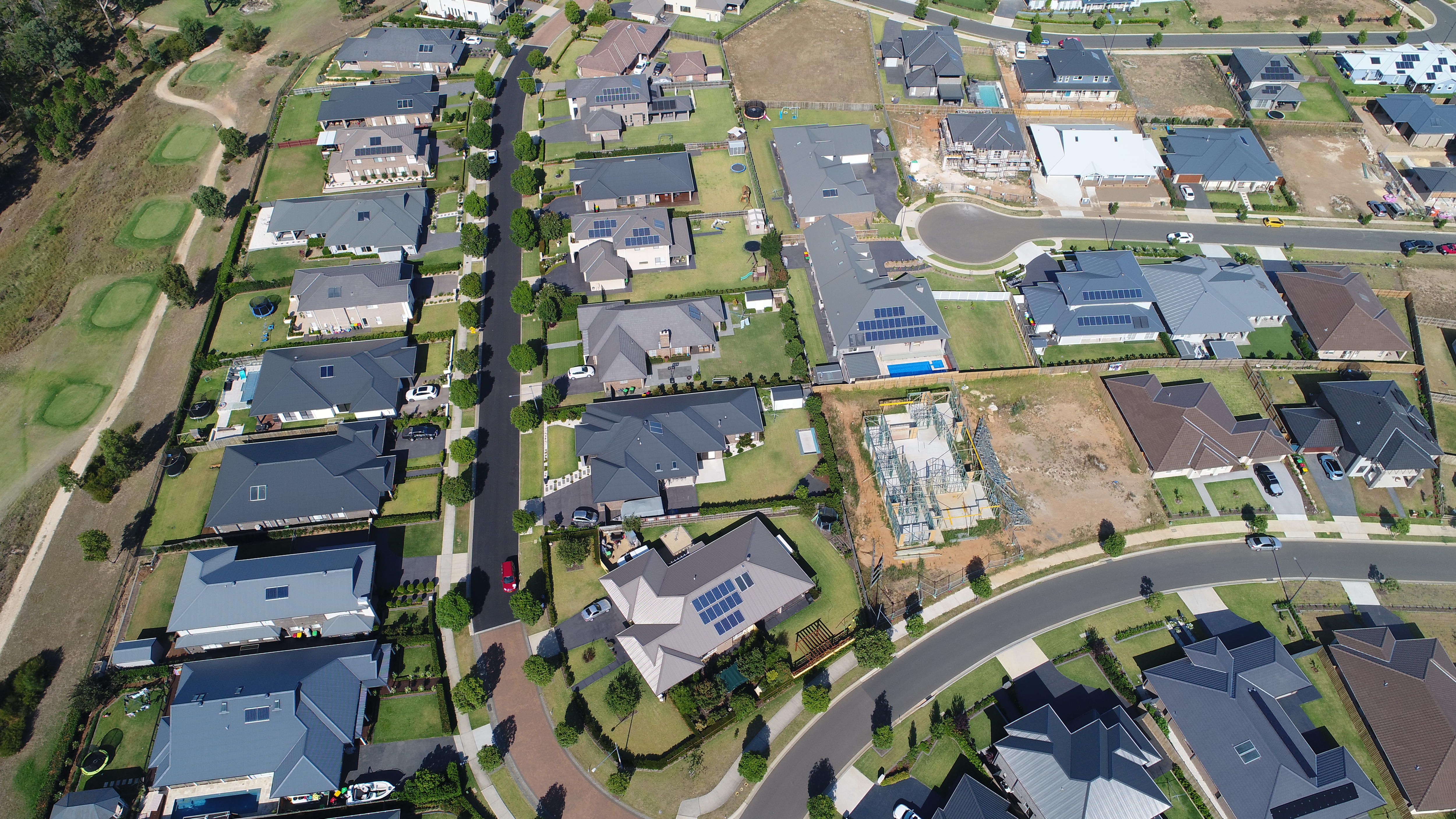 A drone photo of new houses in a suburb, some of which have solar panels of their roofs.