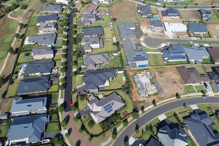 A drone photo of new houses in a suburb, some of which have solar panels of their roofs.