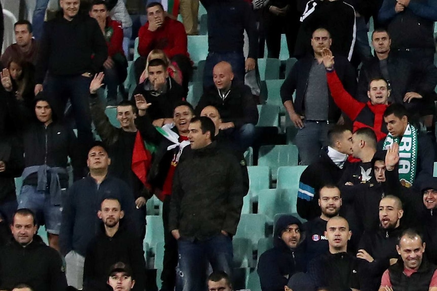 A group of football fans watch a match, with some of them raising their arms in Nazi salutes.