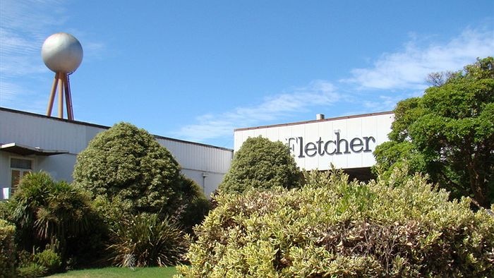 A factory with a spherical-ball shaped tank mounted on a tripod on the roof and with surrounding green gardens