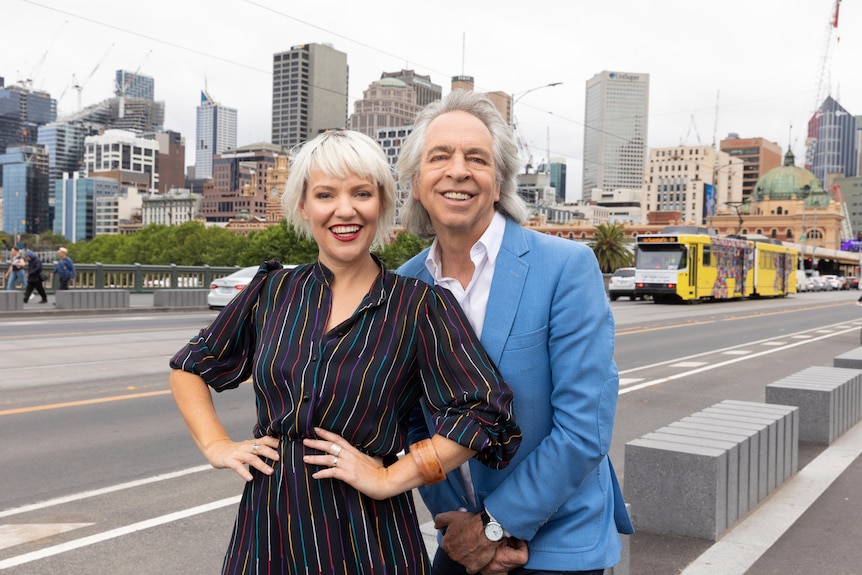 Jacinta Parson and Brian Nankervis standing together smiling on the end of a Melbourne road with city scape in backgroun
