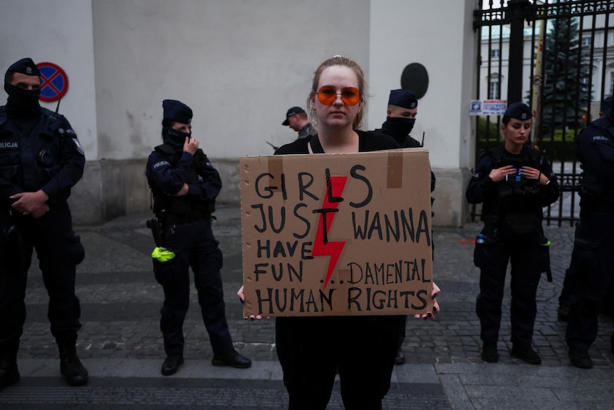 A female protester with red sunglasses holds a sign reading: "girls just wanna have fun…damental human rights".