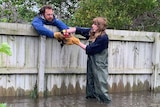 A woman wading in flood waters hands a chicken over a fence to a man.