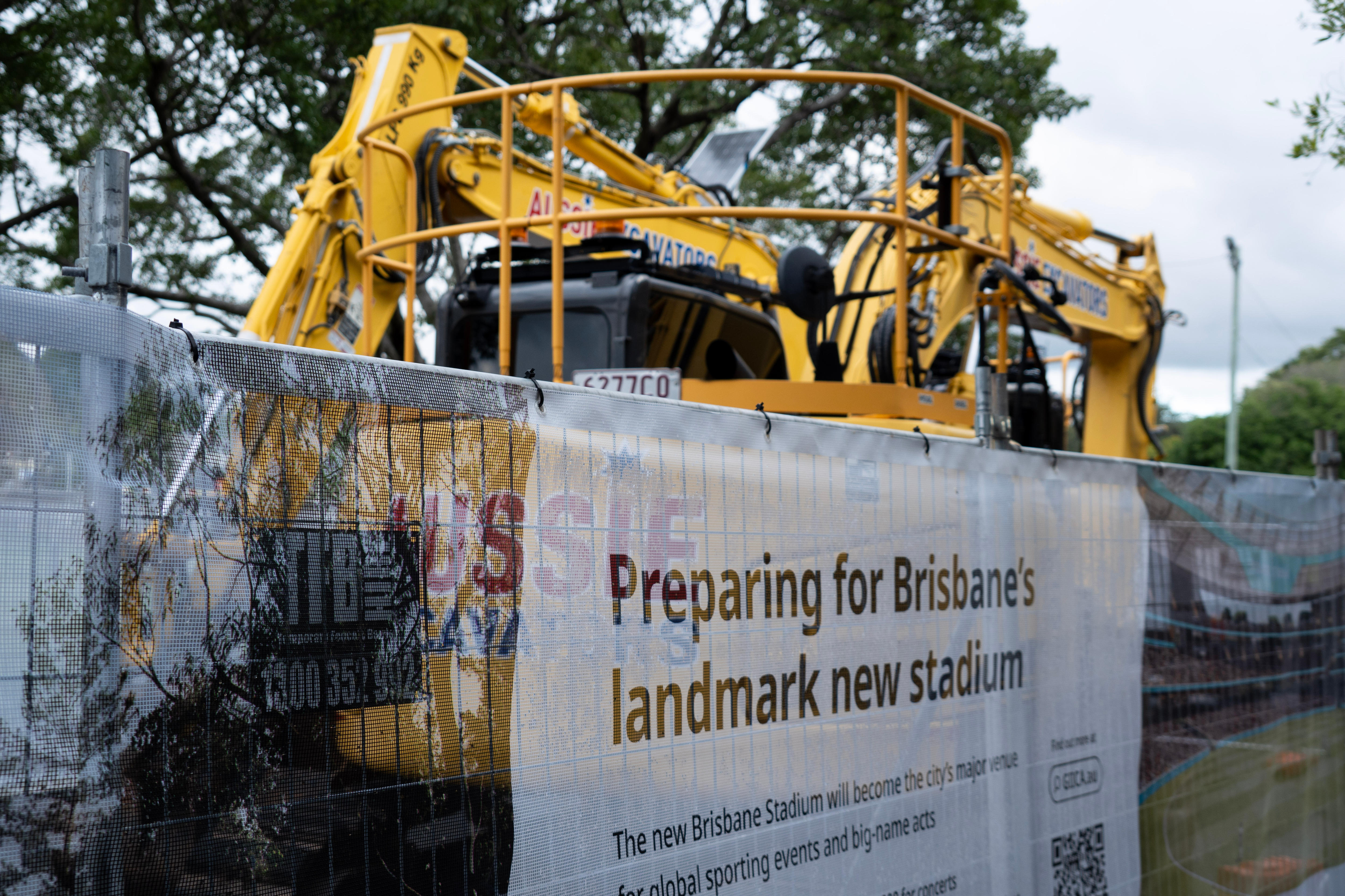 A large yellow excavator behind a fence.