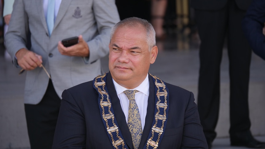 A man with short, grey hair wearing a dark suit and a mayoral ribbon around his neck.