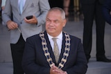 A man with short, grey hair wearing a dark suit and a mayoral ribbon around his neck.