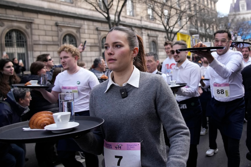 Waitresses and waiters carry trays in a race through the streets of Paris.