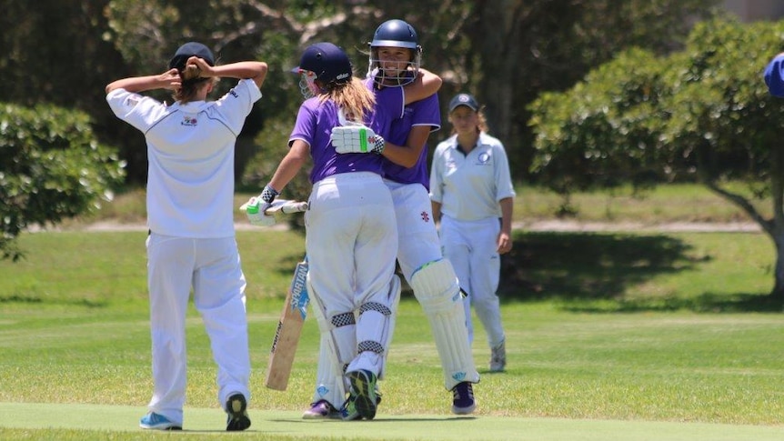 Two young batters celebrate during a game of junior cricket.