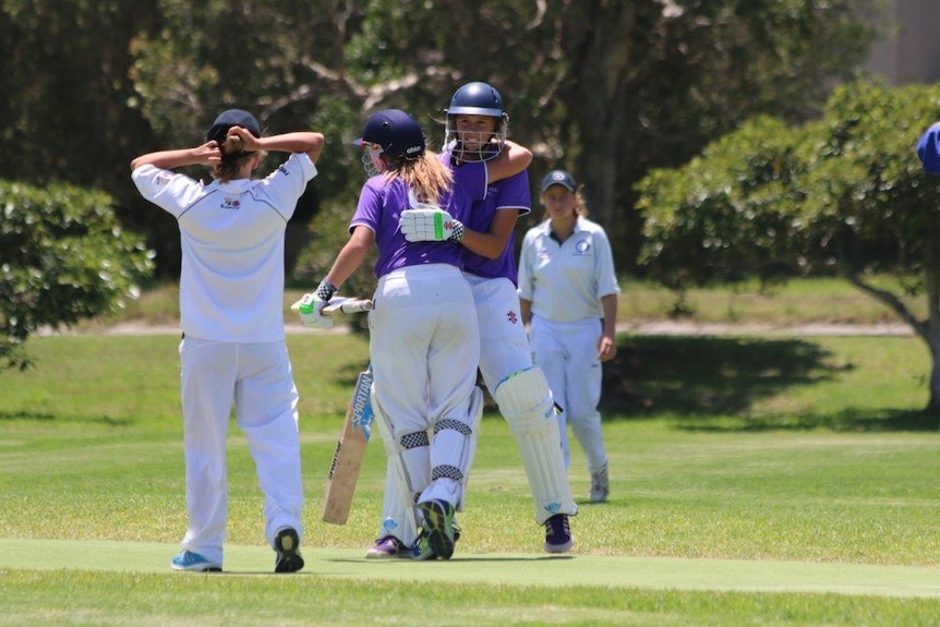 Two young batters celebrate during a game of junior cricket.