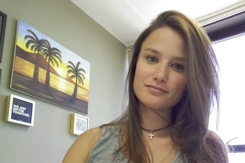 Paula sitting at a desk with a computer keyboard, wearing a grey tank top.