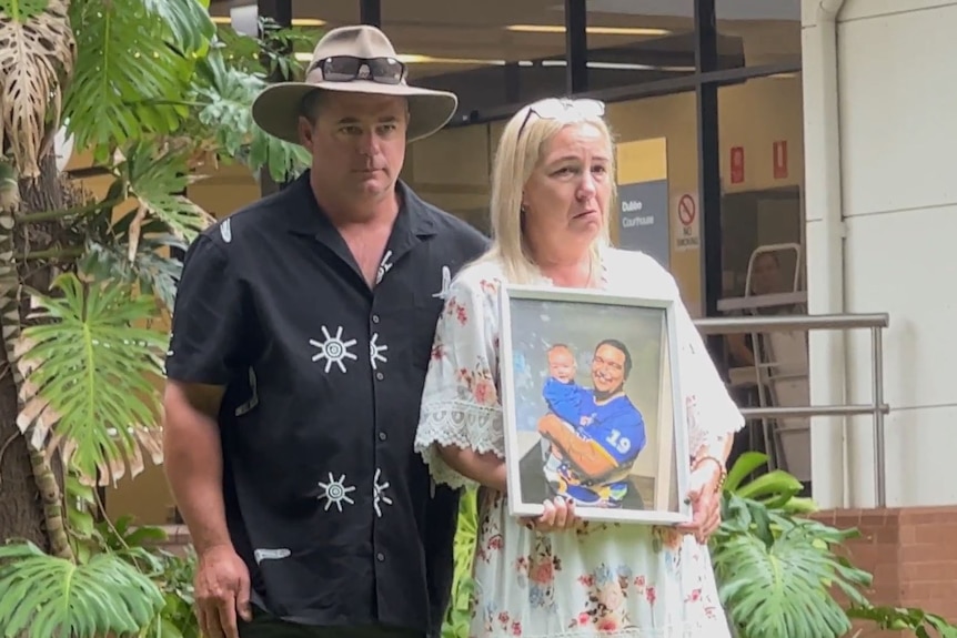 A man and a woman stand holding a photo of their son who died during a police altercation.