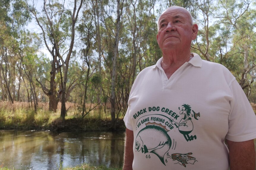 A man stands in front of a billabong wearing a fishing shirt 