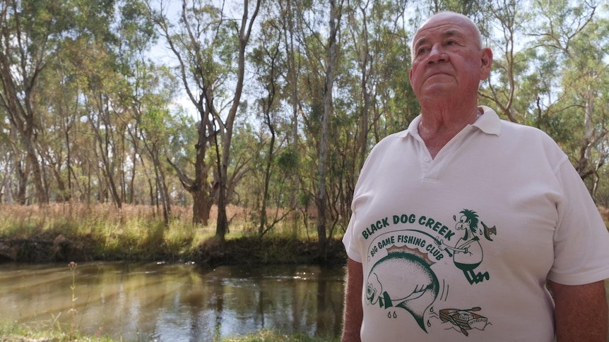 A man stands in front of a billabong wearing a fishing shirt 