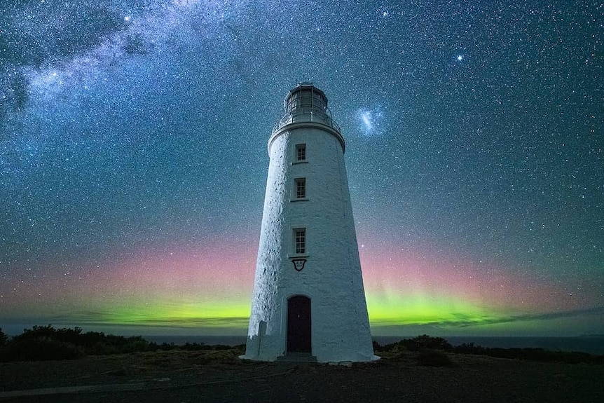 A lighthouse in front of a night sky and the green lights of an Aurora Australia