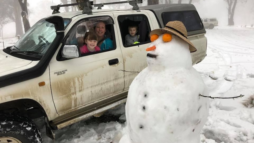 Family in car pose nest to a large and snowman amid a snowy landscape.
