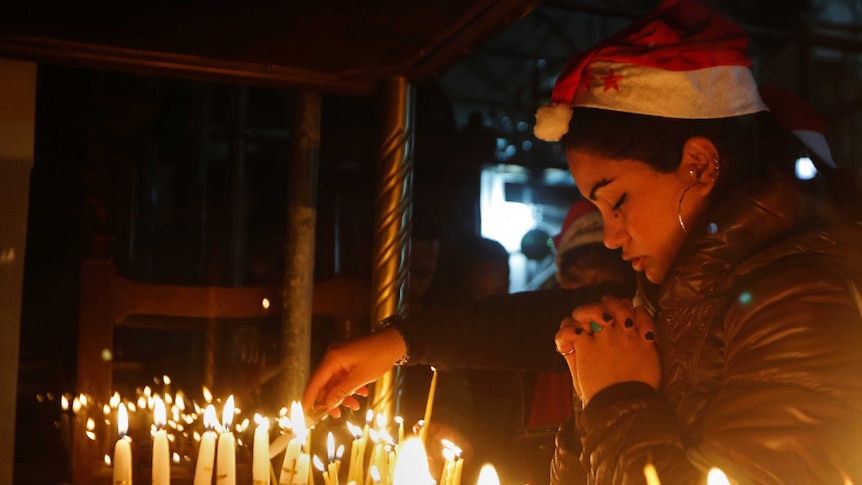 A woman prays before several candles.