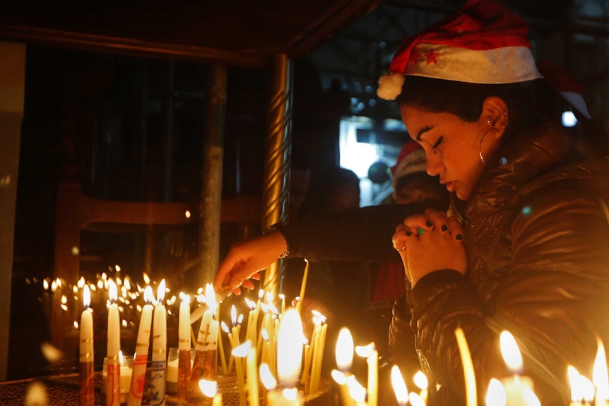 A woman prays before several candles.