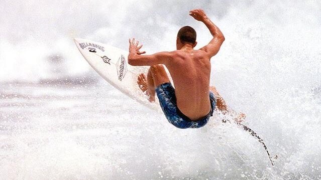 A surfer takes to the air on his board at the top of a wave.